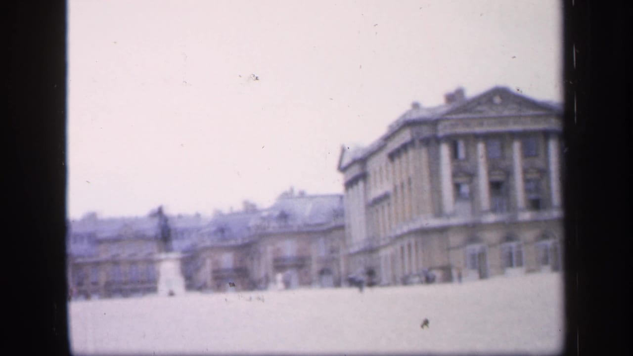 1949 France home-movie frame with a distant statue centered across an open square and a classical stone building at right.