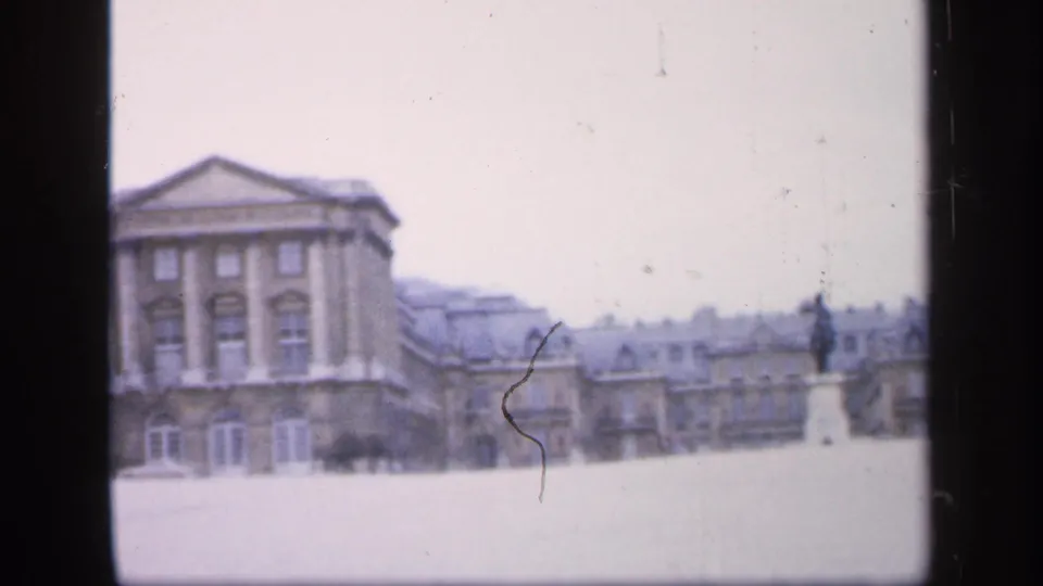 1949 France 8mm frame with a columned corner building in the foreground area and a distant statue beyond the square.