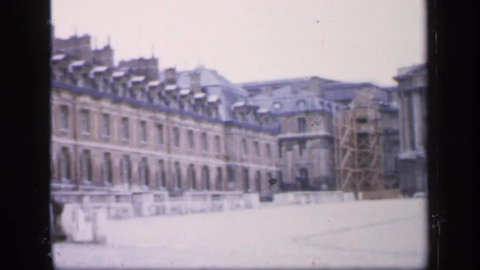 1949 France home-movie view across a snow-covered courtyard toward a long historic wing and scaffolding on the building complex.