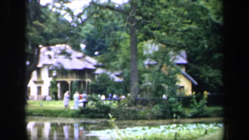 1949 France 8mm frame showing a large house across a pond, with mature trees, lawn, and small groups of people on the grounds.