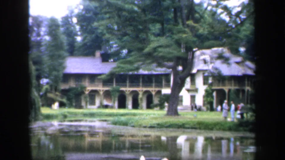 1949 France 8mm frame with a wide view across the pond toward a large house, mature trees, lawn, and distant visitors in light clothing.