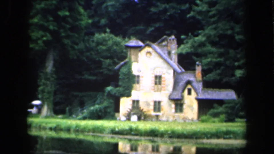 Final 1949 France frame holds on the ivy-covered cottage across the pond, with trees behind it and a small indistinct person or object near the left bank.