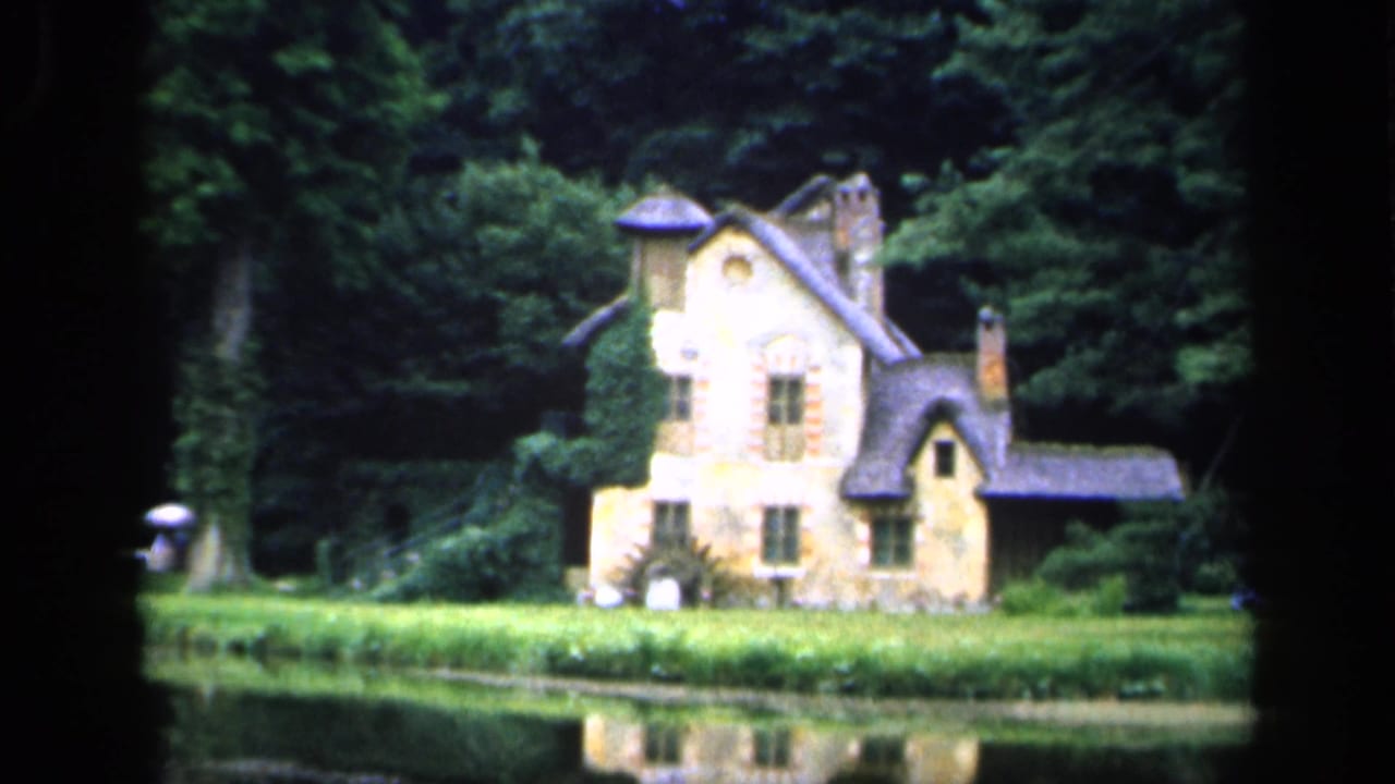 1949 France 8mm frame showing a small stone chateau across a reflective pond, bordered by lawn and dense trees.