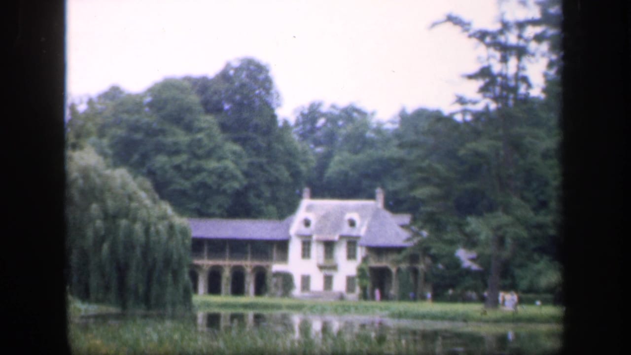 French 1949 home-movie view of the chateau, pond reflection, willow, and surrounding trees, framed by the 8mm scan edge.