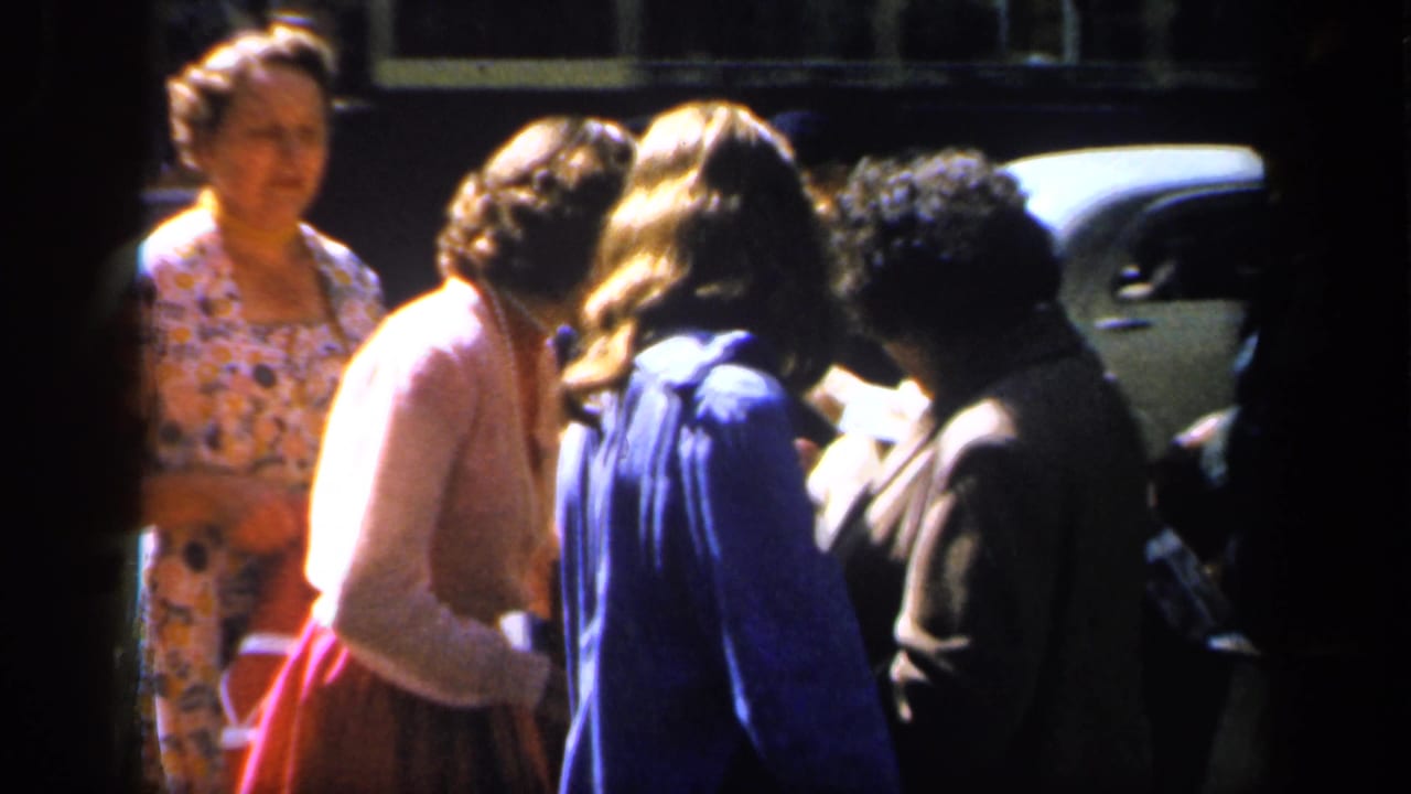 Several women stand close together beside a parked car on the street.