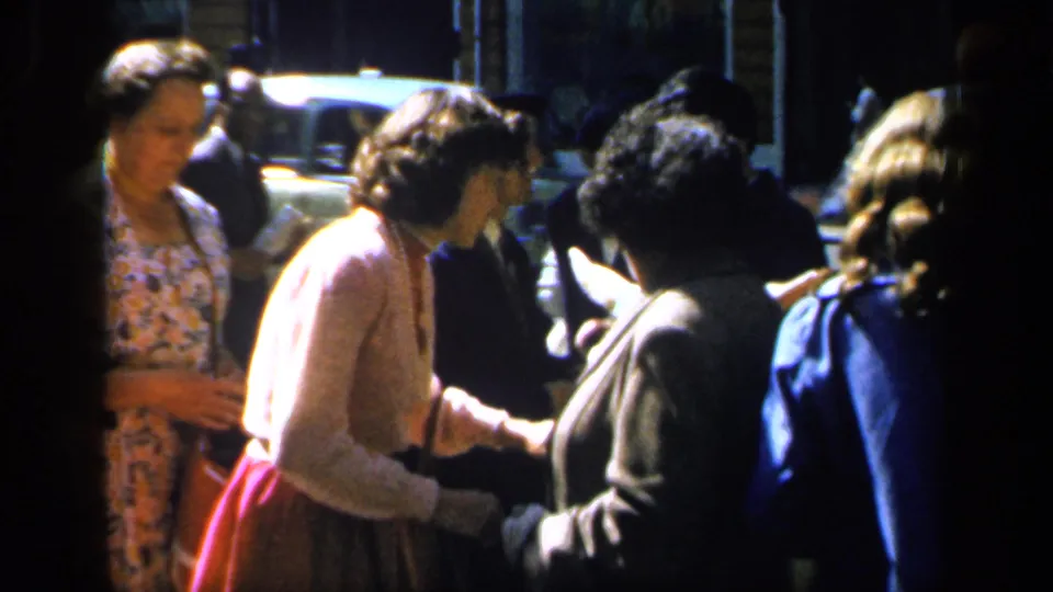 1949 France home-movie frame of women in mid-century clothing grouped on a sunny street near cars and pedestrians.