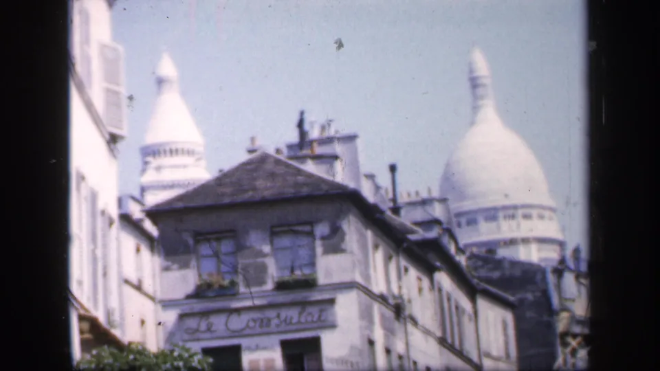 1949 Paris home-movie frame with weathered facades, window shutters, rooftops, and Sacré-Cœur rising behind the street.