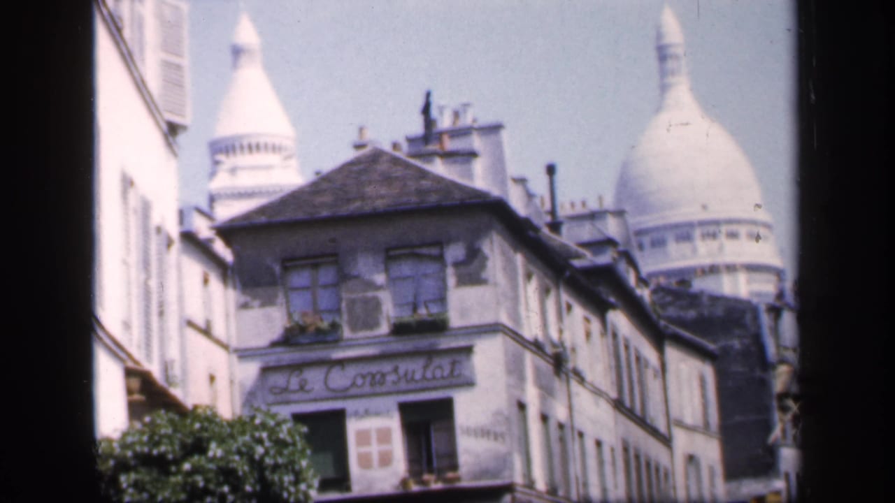 Le Consulat building with Sacre-Coeur dome rising behind it on a Paris street.
