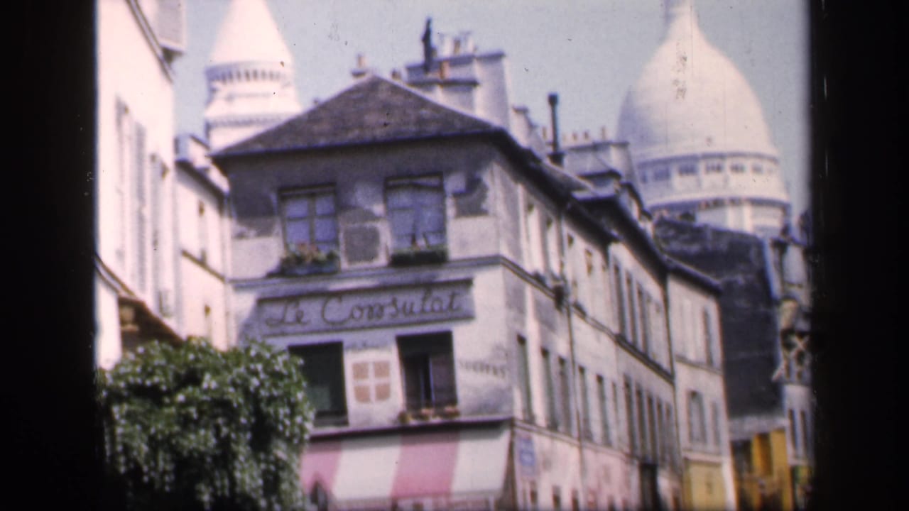 Paris street corner with Le Consulat sign and Sacre-Coeur dome in the background.