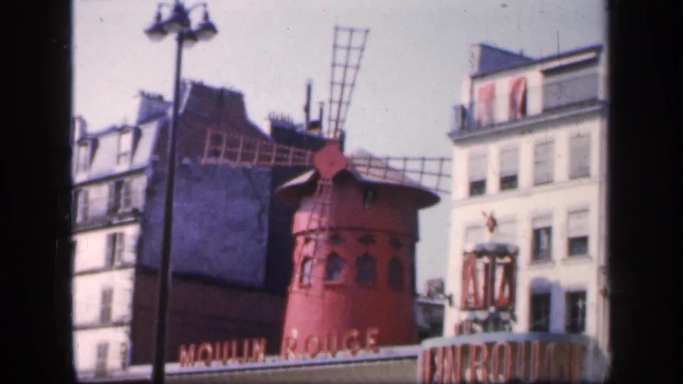 1949 France home-movie frame showing the red Moulin Rouge windmill and nearby buildings in Paris.