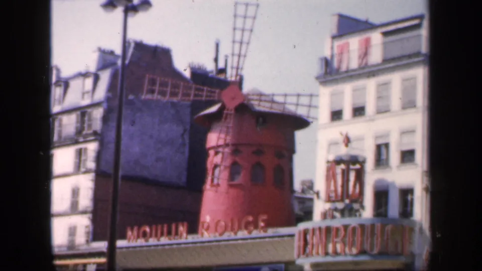 1949 8mm view of the Moulin Rouge windmill, entrance signage, nearby buildings, and street poles in Paris.