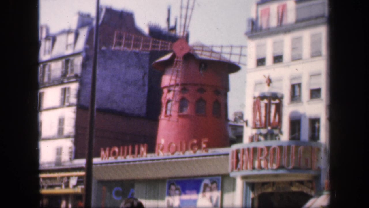 Moulin Rouge facade with red windmill, entrance sign, buildings, and street activity.