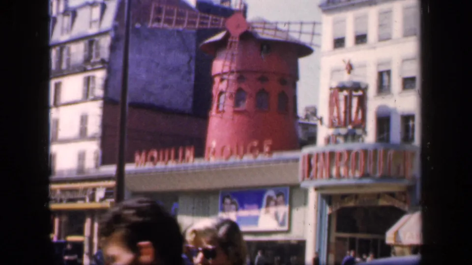 1949 8mm frame of the Moulin Rouge exterior in Paris, with the windmill, entrance letters, posters, and foreground pedestrians.