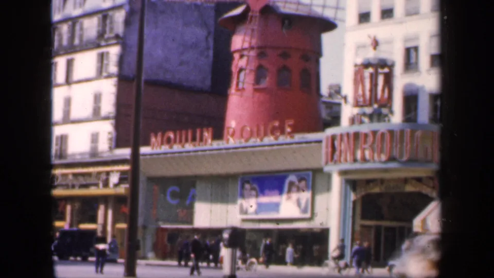 1949 Paris view of the Moulin Rouge facade, red windmill, entrance signage, pedestrians, cars, and surrounding urban buildings.