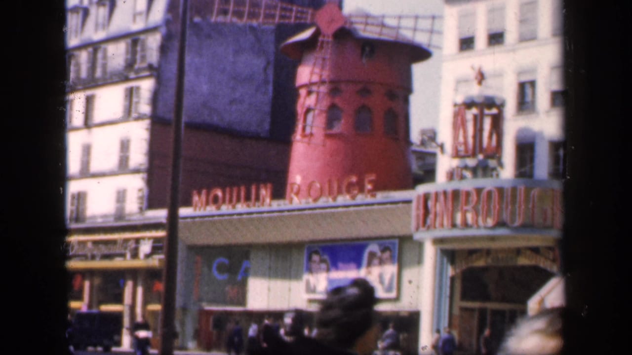 Moulin Rouge exterior with red windmill, entrance signage, Paris buildings, and pedestrians at street level.