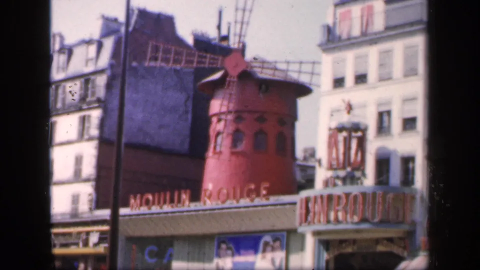 1949 Paris street view of the Moulin Rouge, with soft-focus 8mm texture, red windmill structure, signage, posters, and pedestrians below.