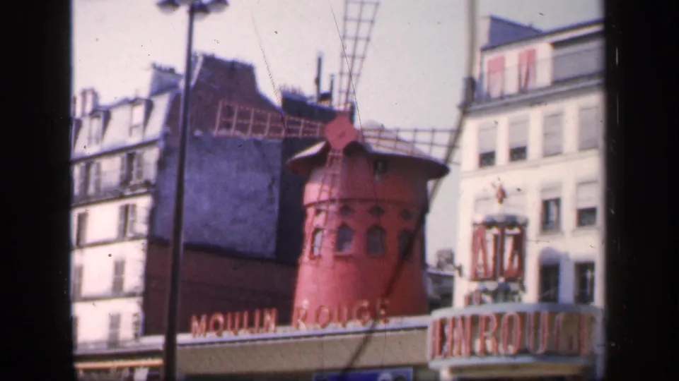 1949 Paris home-movie frame showing the Moulin Rouge windmill, partial signage, and surrounding multi-story buildings.