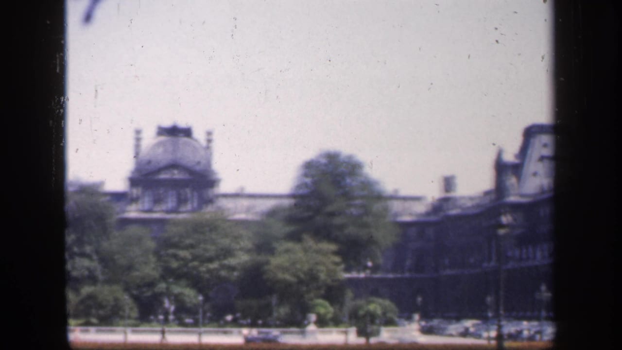 Historic building seen past trees through a dark window-frame edge.