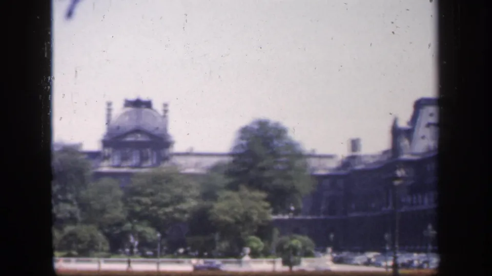 1949 France home-movie frame showing a distant ornate building and trees, partly blocked by dark window-frame borders.