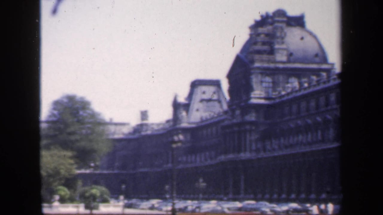 1949 France exterior view of a long ornate stone facade with mansard roofs, trees, parked cars, and dark frame borders.