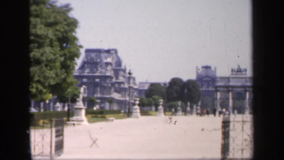 1949 France home-movie frame looking toward a large chateau-like building beyond statues, trees, gates, and garden paths.