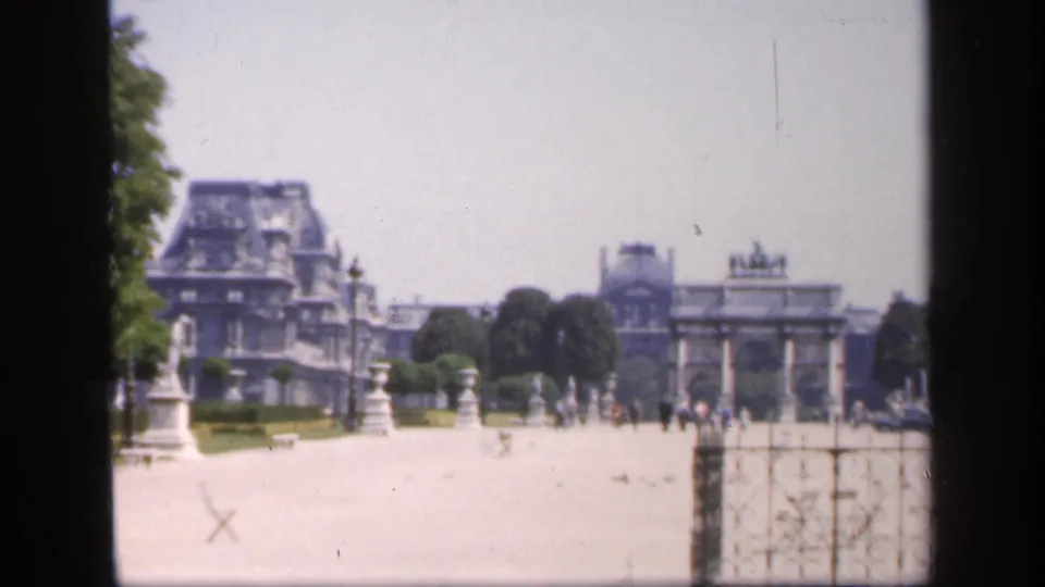 1949 France home-movie view of formal garden grounds with visitors, statues, gates, trees, and a distant chateau-like facade.