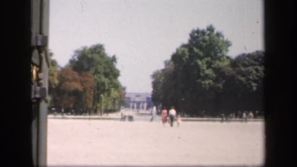 Wide 1949 France home-movie view of a paved public area lined with trees, with distant pedestrians and soft faded color.