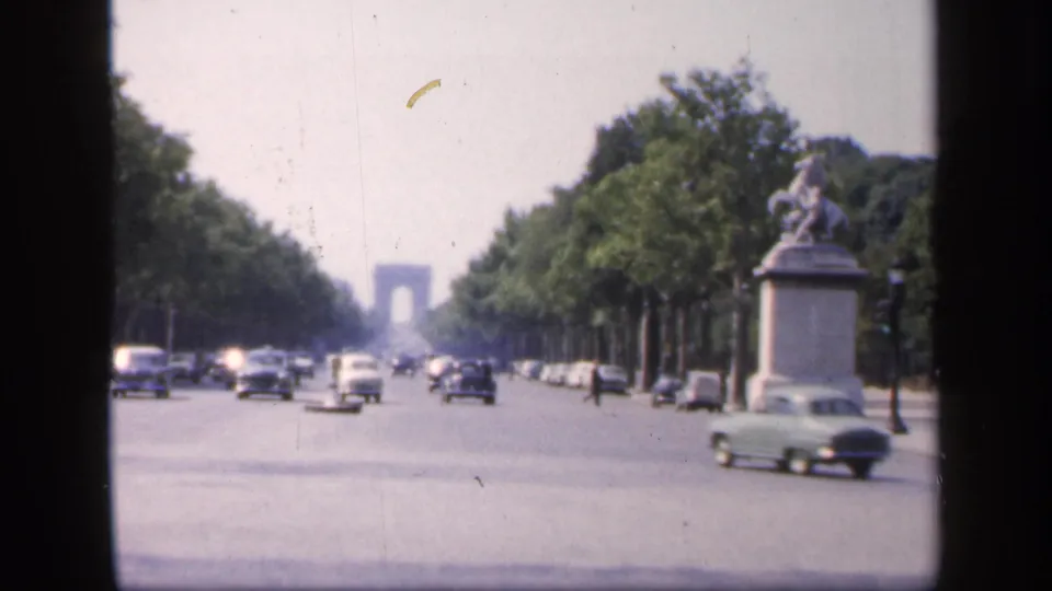 1949 France street view showing a broad tree-lined boulevard, mid-century cars, pedestrians, a statue at right, and a distant arch-like form.
