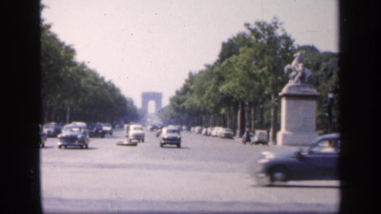 Classic cars travel along a broad tree-lined boulevard with the Arc de Triomphe centered in the distance.