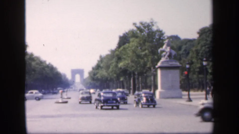 Final 1949 Paris street frame with heavier foreground traffic, a right-side equestrian monument, tree-lined sidewalks, and the distant Arc de Triomphe.