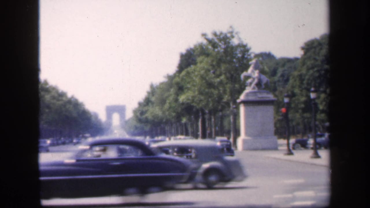 1949 Paris boulevard traffic with late-1940s cars, trees, traffic lights, and the Arc de Triomphe in the distance.