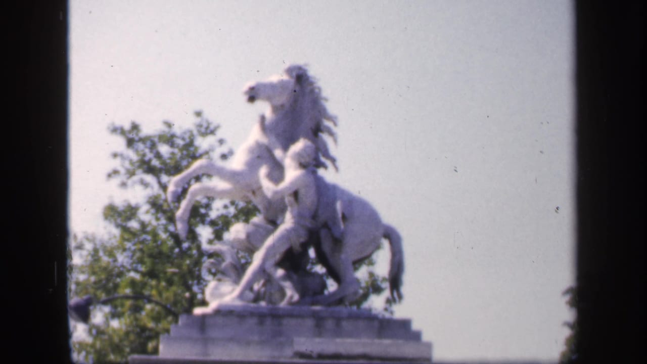 White rearing horse and rider statue on a pedestal against sky and trees.