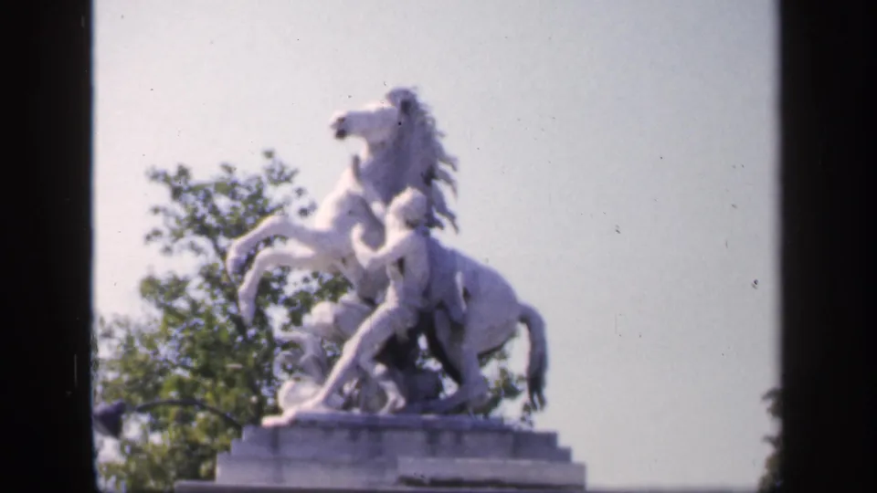 1949 France 8mm frame showing a white equestrian statue on a stone pedestal with bright sky and trees behind it.