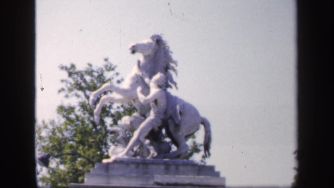 Equestrian statue centered between dark film borders with trees behind.