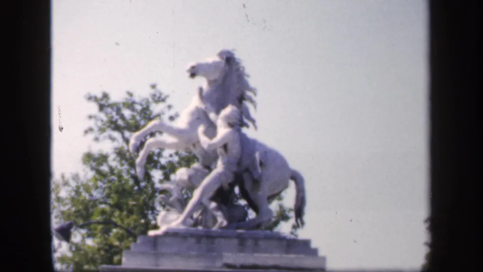 1949 France home-movie still of a pale horse-and-rider monument framed by dark 8mm borders and greenery.