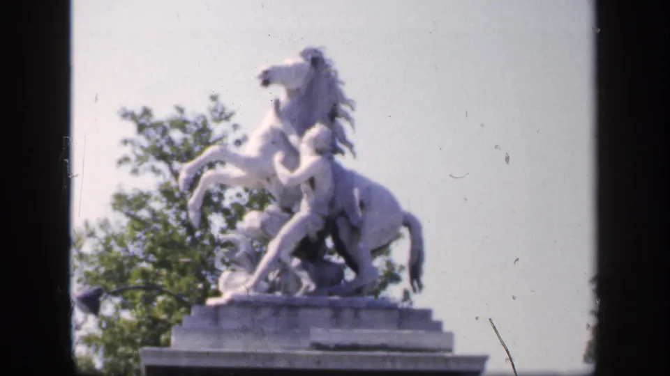 Final 1949 France frame of the white equestrian statue, with the stone pedestal, leafy background, and visible film wear.