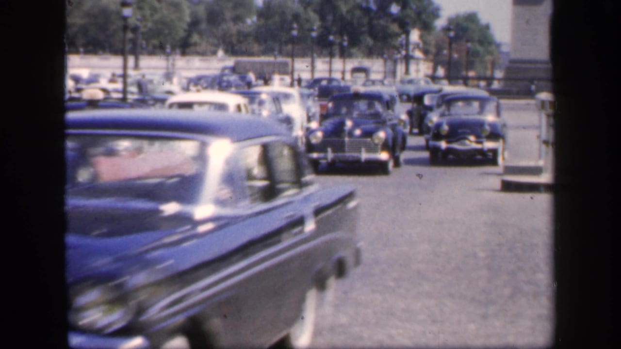 A blue car passes close to the camera as other vintage cars approach behind it.