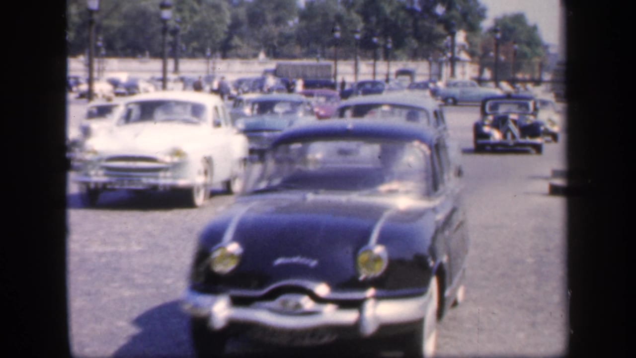 Vintage cars driving toward the camera on a broad city avenue.