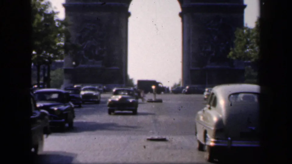 1949 Paris street view with vintage cars heading toward the Arc de Triomphe, seen through soft home-movie framing.
