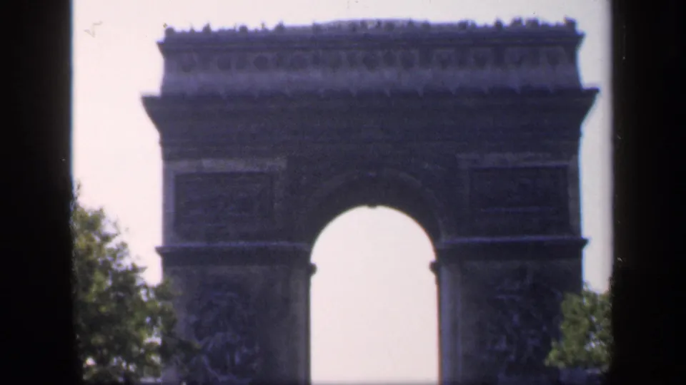 Vintage 8mm frame of the Arc de Triomphe in Paris, with the monument cropped by dark vertical framing and boulevard trees.