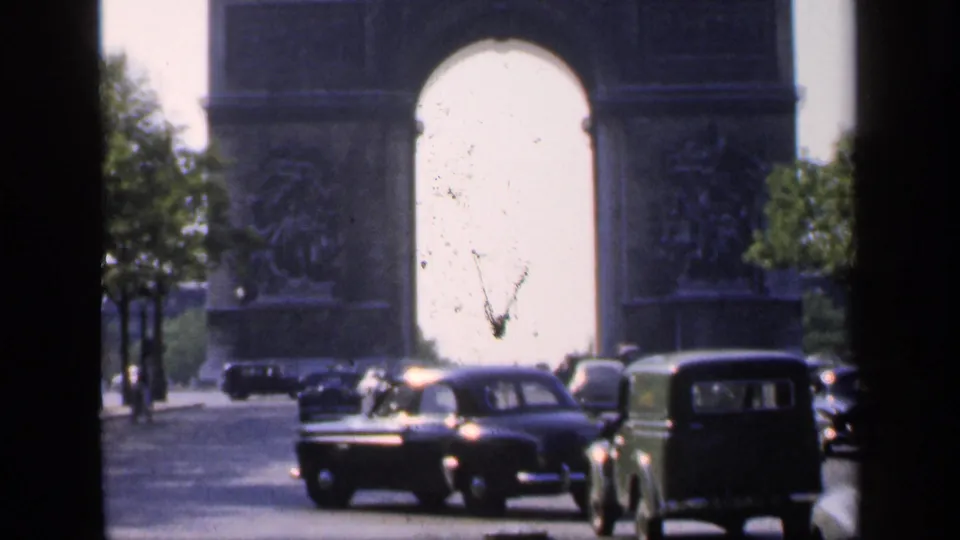 1949 Paris street view with classic cars and a green van passing in front of the Arc de Triomphe.