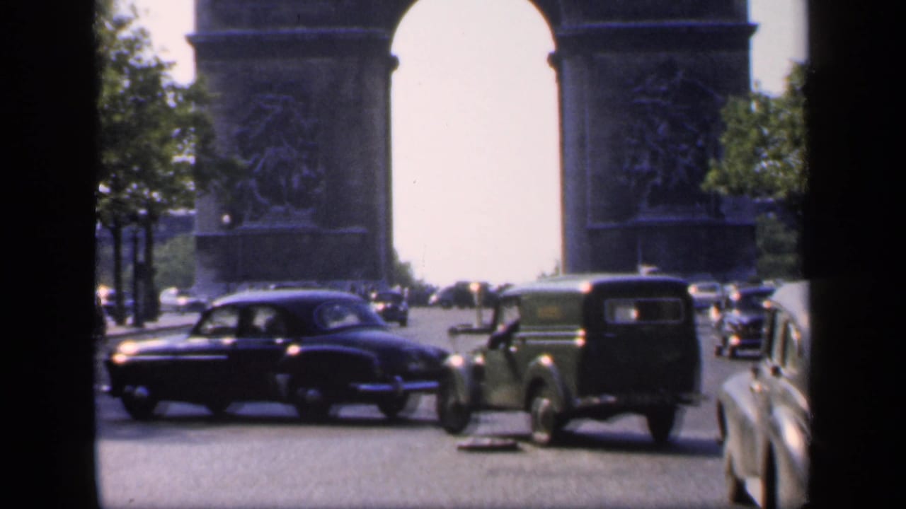 1949 Paris home-movie frame showing the Arc de Triomphe, passing automobiles, trees, and bright daylight.