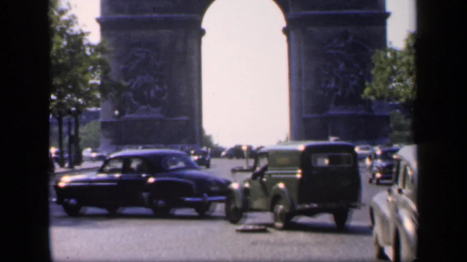 1949 Paris home-movie frame showing the Arc de Triomphe, passing automobiles, trees, and bright daylight.