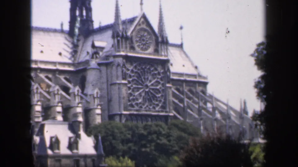 1949 France home-movie view of Notre Dame's Gothic facade, rose window, buttresses, trees, and pale sky.