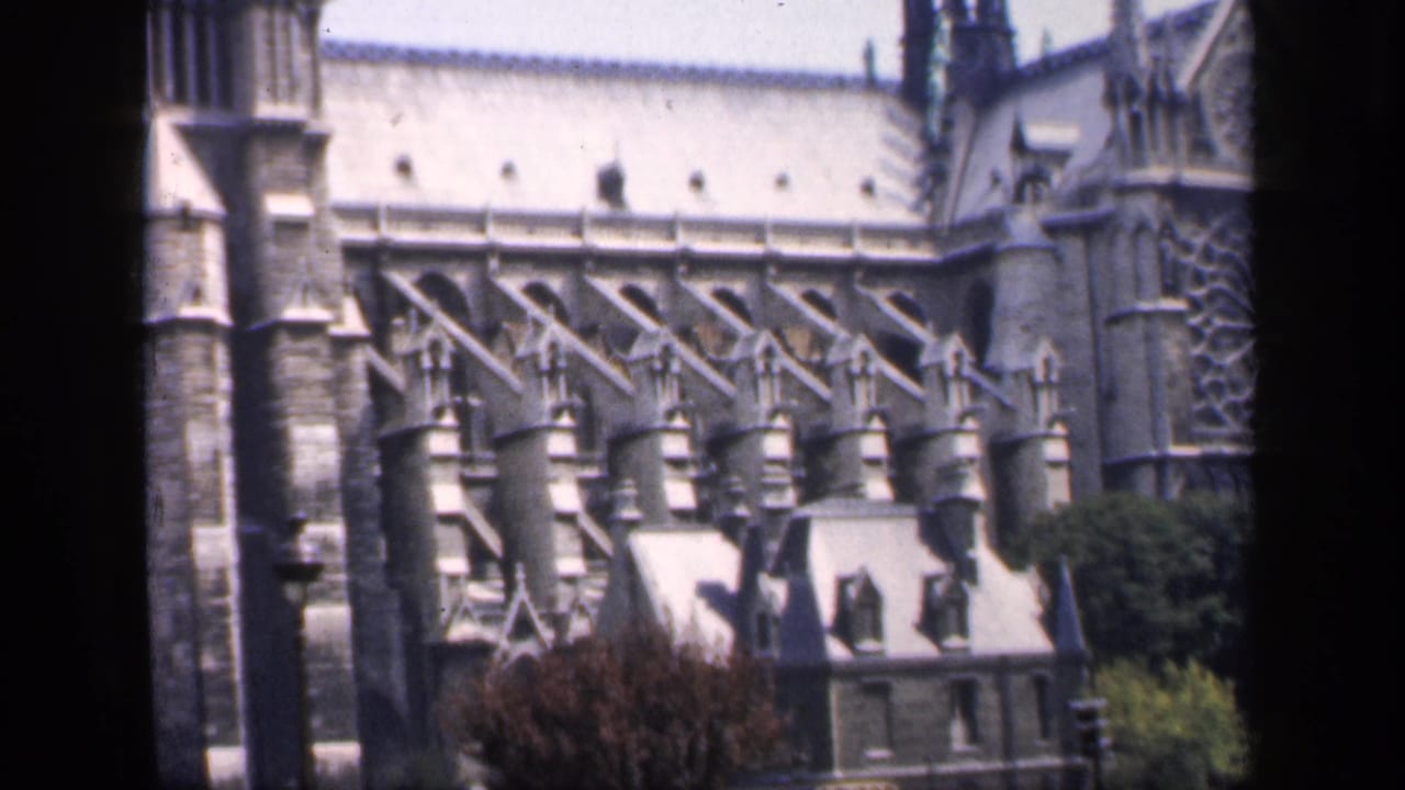 Notre-Dame side elevation with buttresses, stone roofline, spires, trees, and a small foreground building.