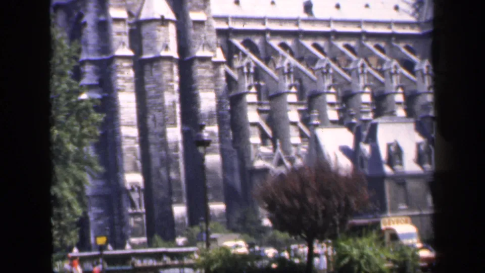 1949 France frame showing Notre-Dame's buttressed exterior with trees and street-level vehicles partly visible in the foreground.