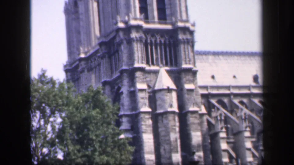 1949 France 8mm still showing Notre-Dame tower stonework, buttresses, roofline, and a large tree in the foreground.