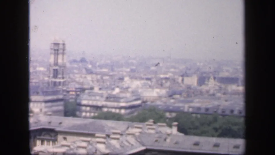 1949 8mm Paris skyline view with rooftops, haze, a tall tower structure, and distant city buildings.