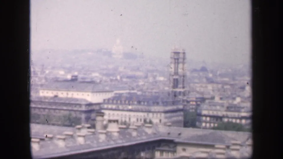 1949 8mm Paris skyline with foreground roofs, a tall tower structure, distant domes, and visible film grain.