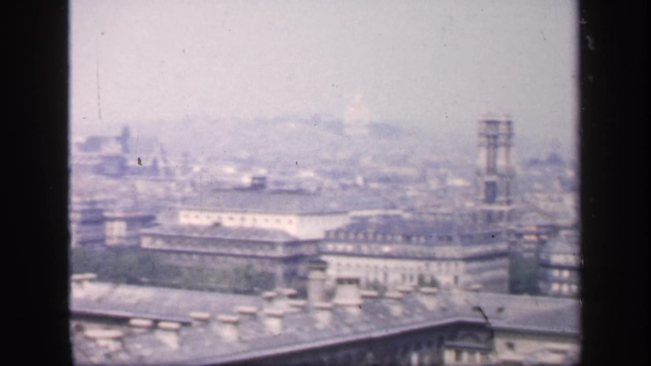 Hazy elevated view over French city rooftops with a tower and dark vertical foreground bars.